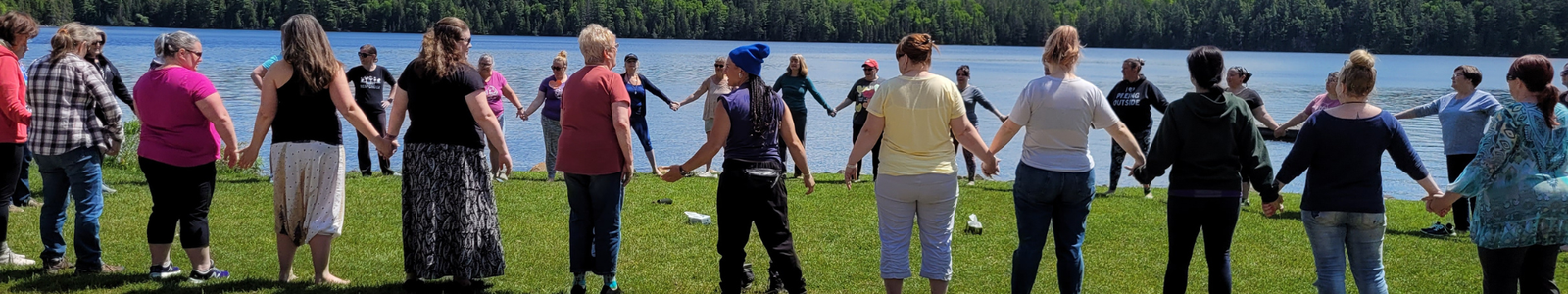 Women holding hands in a large circle by the lake at a women's wellness retreat in Ontario, Canada