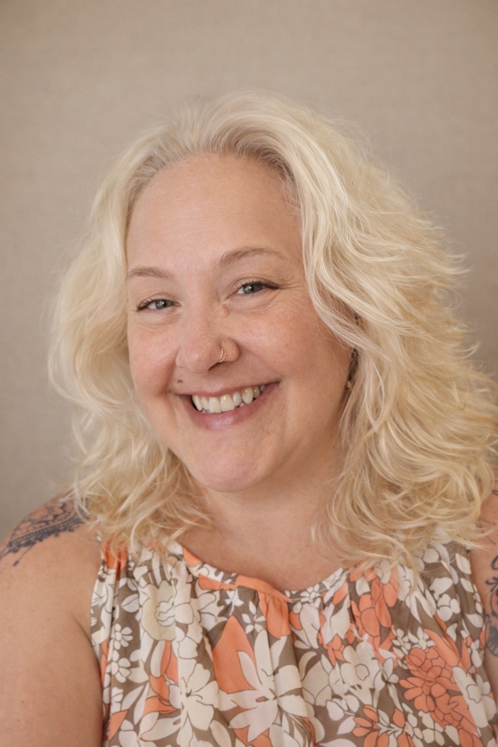 Smiling woman with wavy blonde hair wearing an orange floral top.