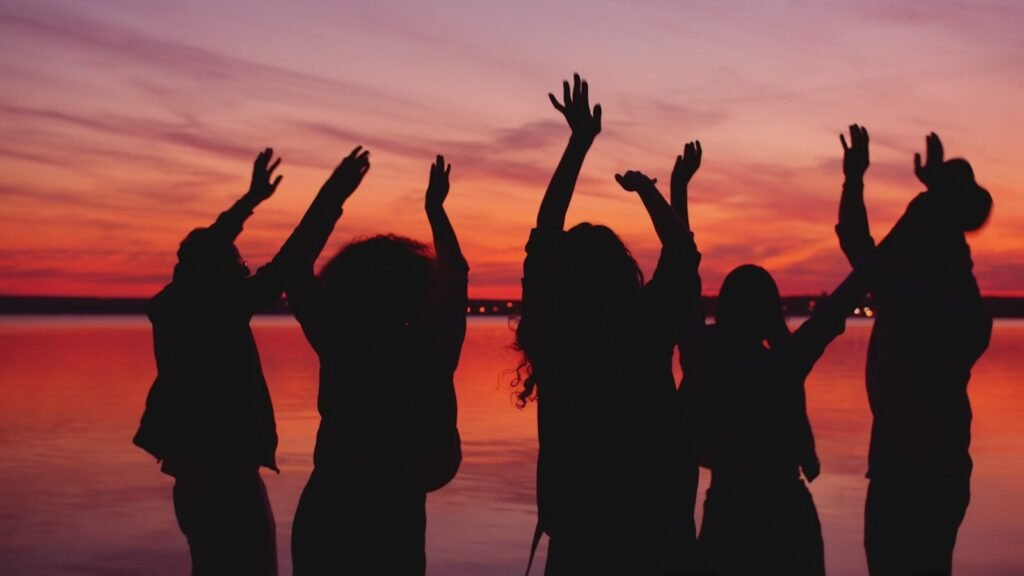 Silhouettes of people dancing at sunset by the water