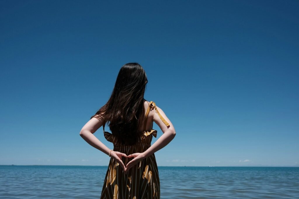 a woman standing in the water making a heart shape with her hands
